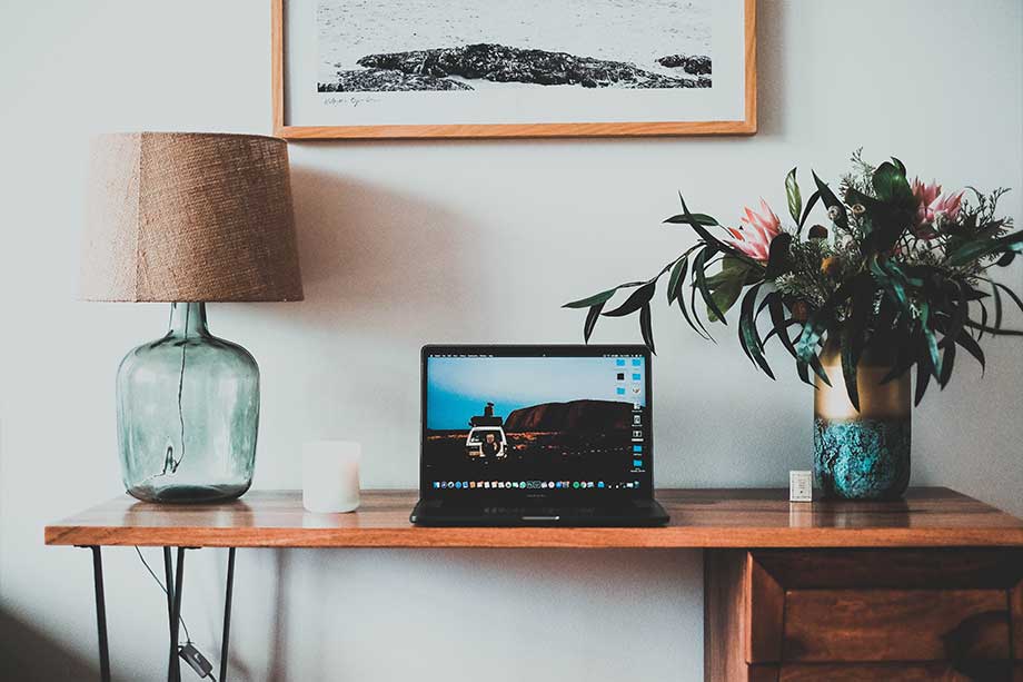 Laptop on a table with flower pot and frame on the wall